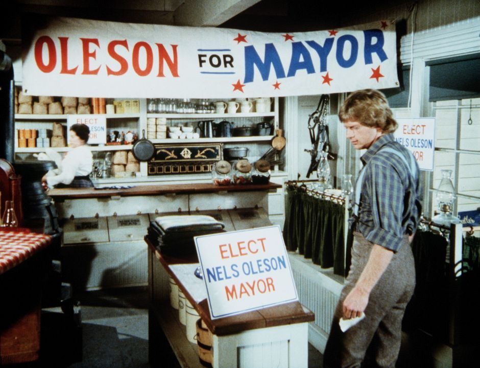 Almanzo (Dean Butler, r.) kommt zu Mrs. Oleson (Katherine MacGregor, l.) in den Laden und erfährt, dass er ebenfalls für das Bürgermeisteramt kan... - Bildquelle: Worldvision